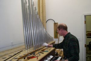 Technician tuning organ pipes at keyboard
